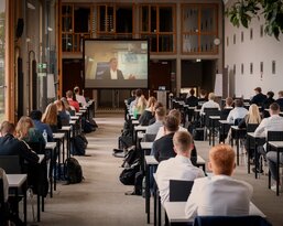 A group of students is sitting in a classroom, following a presentation on a large screen. The desks are arranged in rows, and the participants are focused on what’s happening on the screen.